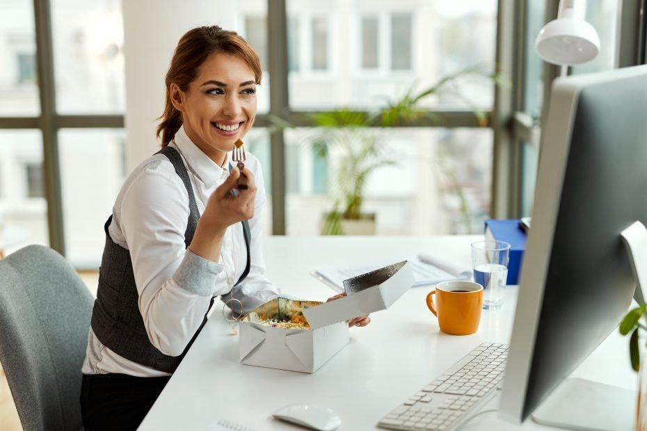 Young happy businesswoman using computer while having lunch break in the office.